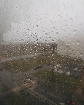 Close-up of raindrops on window creating a blurred view of an urban landscape.