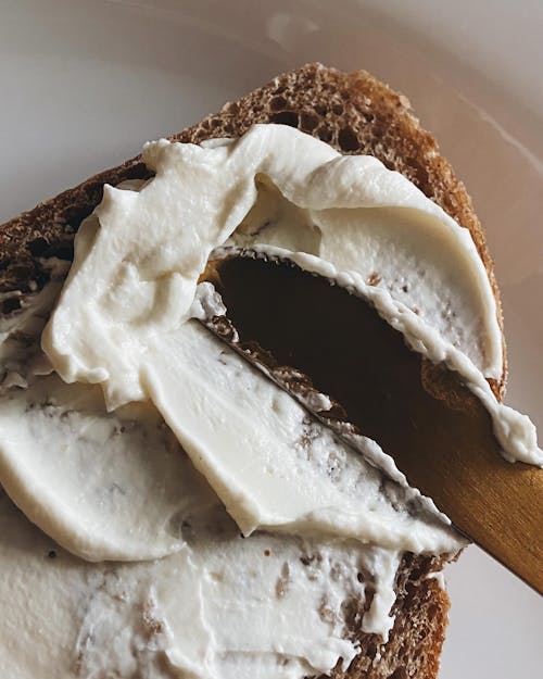 A knife is cutting a piece of bread with cream