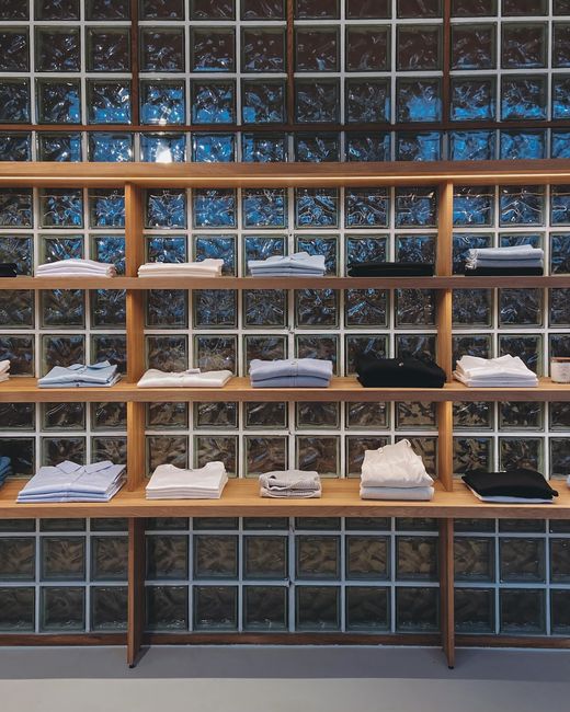 Miljöbild – Organized display of folded shirts on wooden shelves against a glass block wall.