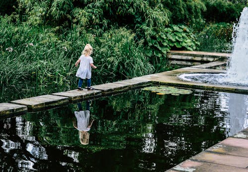 A little girl is standing on a bridge over a pond