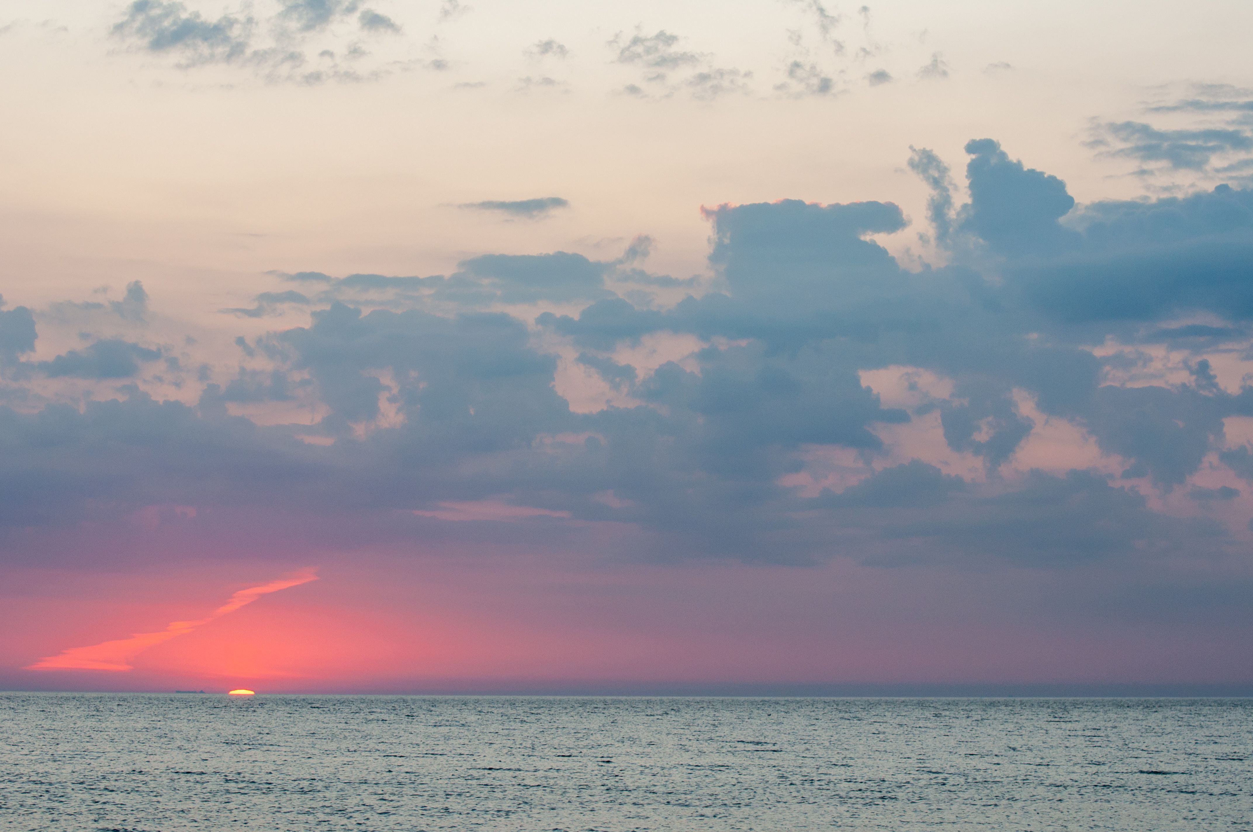 A sunset over the ocean with clouds in the sky · Free Stock Photo
