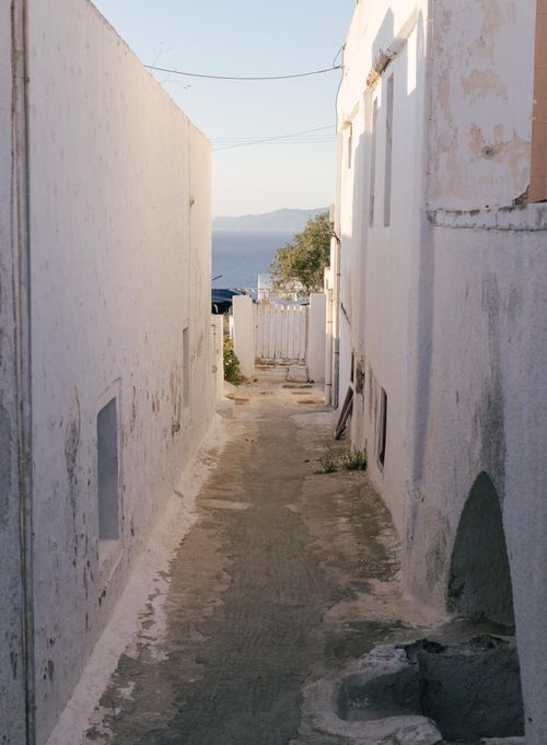 Free A narrow alley with whitewashed buildings leading to a serene ocean view. Stock Photo