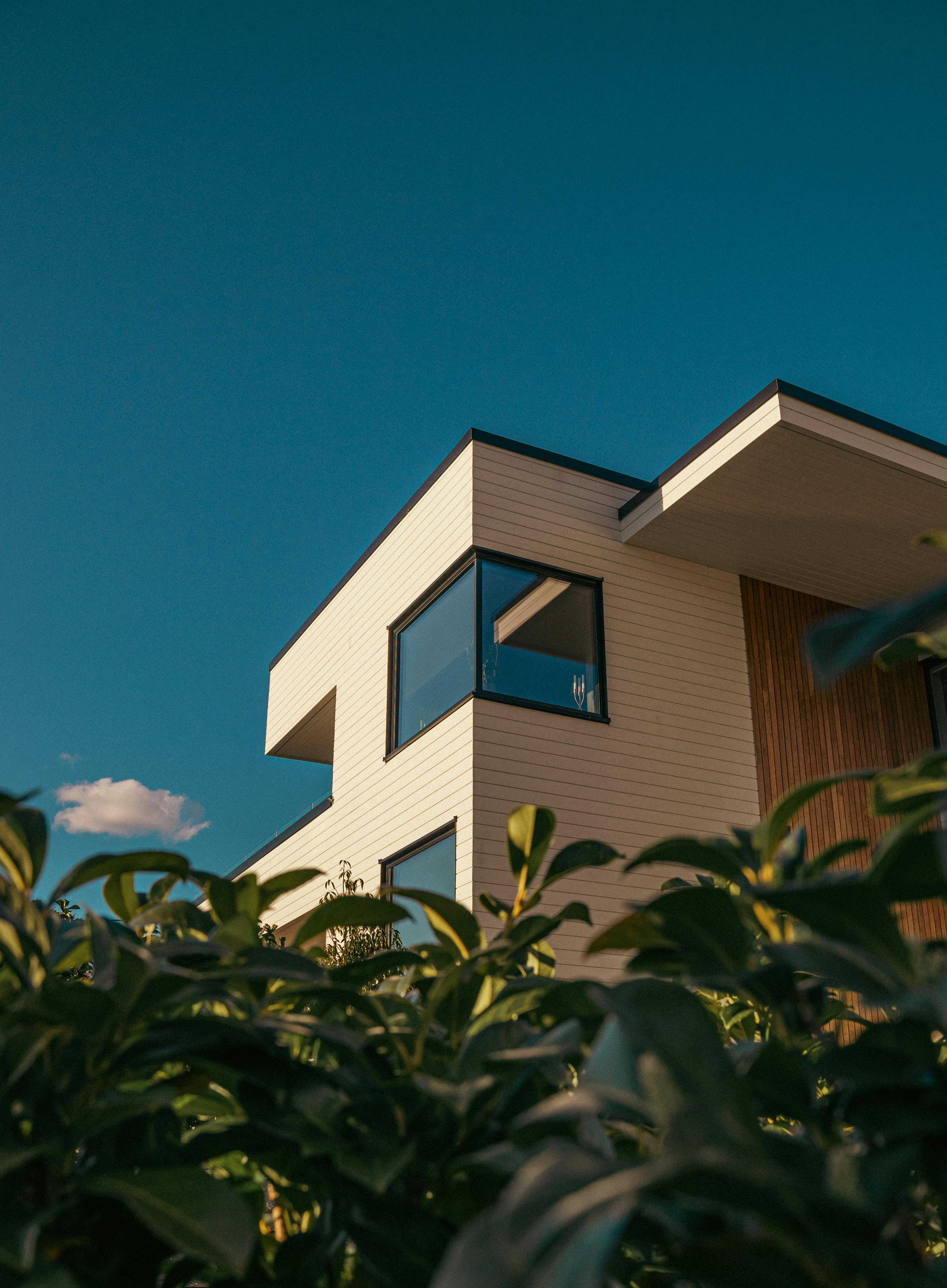 Elegant modern house with large windows and a clear sky background, framed by greenery.