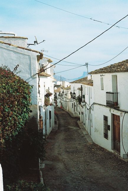Idyllic narrow street with traditional white houses in a Mediterranean village, under a clear blue sky.