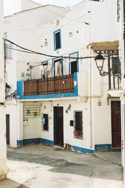 A picturesque whitewashed house with blue accents and a balcony in a Mediterranean village.
