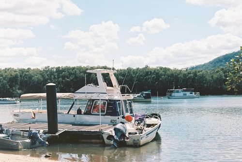 Free Idyllic view of motorboats moored at a pier on a serene lake surrounded by lush trees and distant hills. Stock Photo