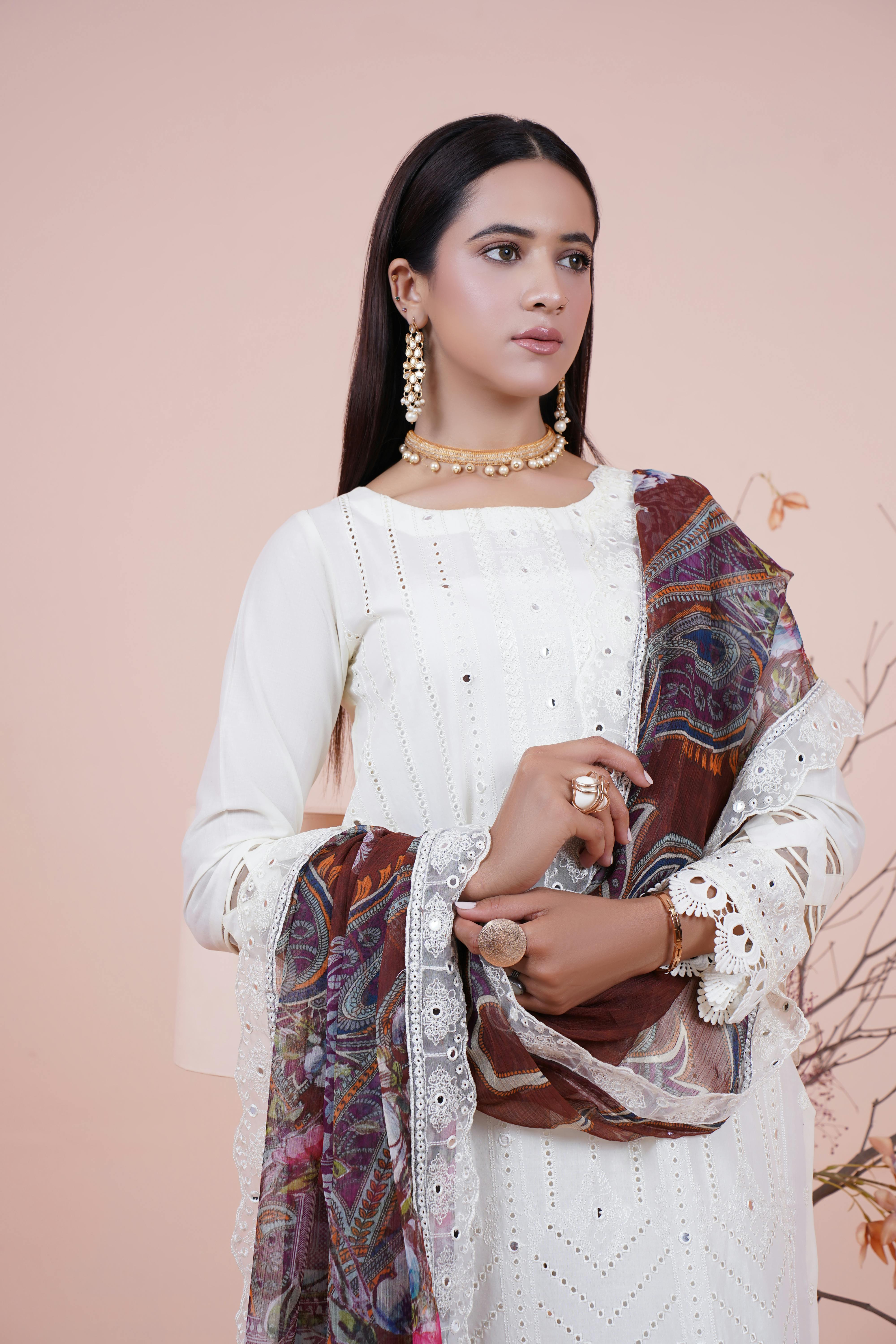 Portrait of a woman in white traditional dress and jewelry posing with scarf indoors.