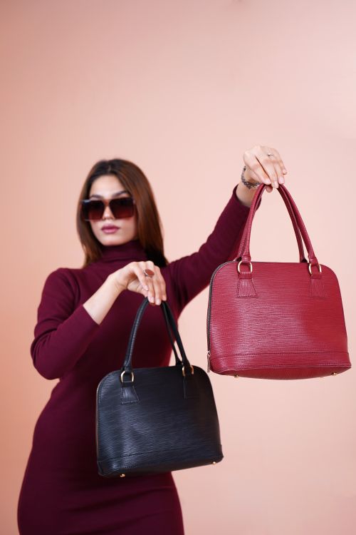 Free A stylish woman in sunglasses displays elegant red and black handbags in a studio shoot. Stock Photo