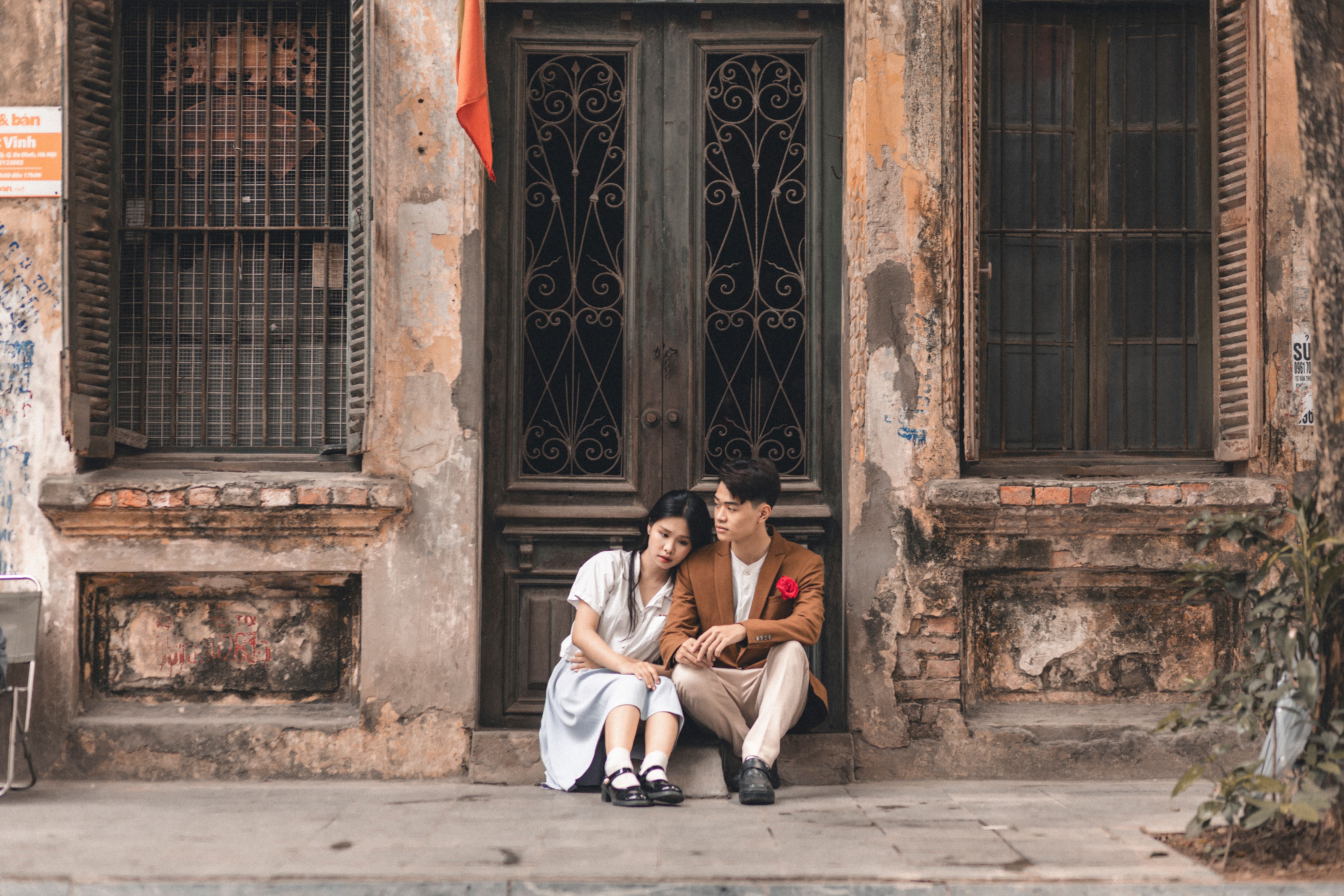 A couple sitting together against a rustic building exterior, creating a romantic urban scene.