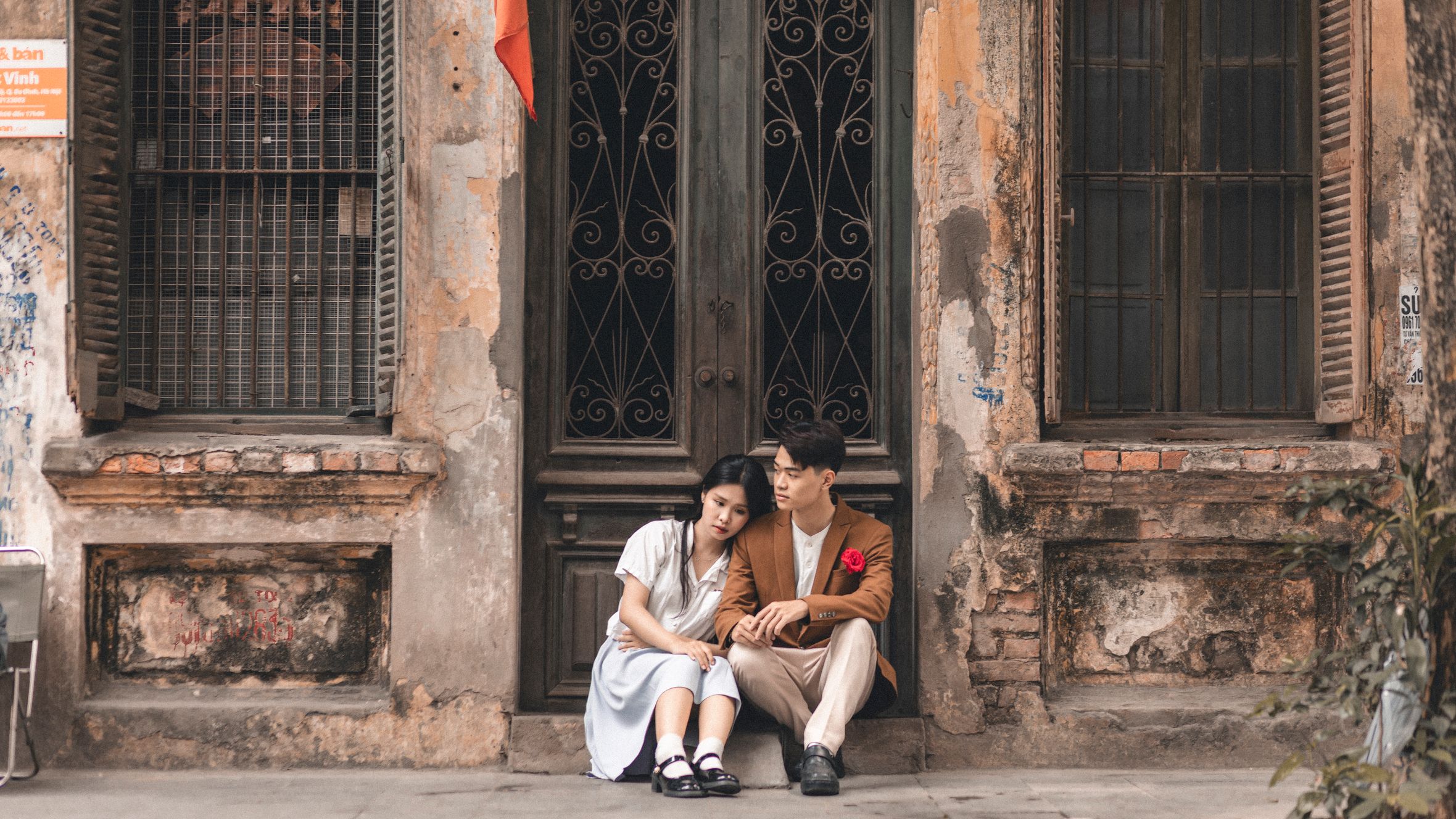 A couple sitting together against a rustic building exterior, creating a romantic urban scene.