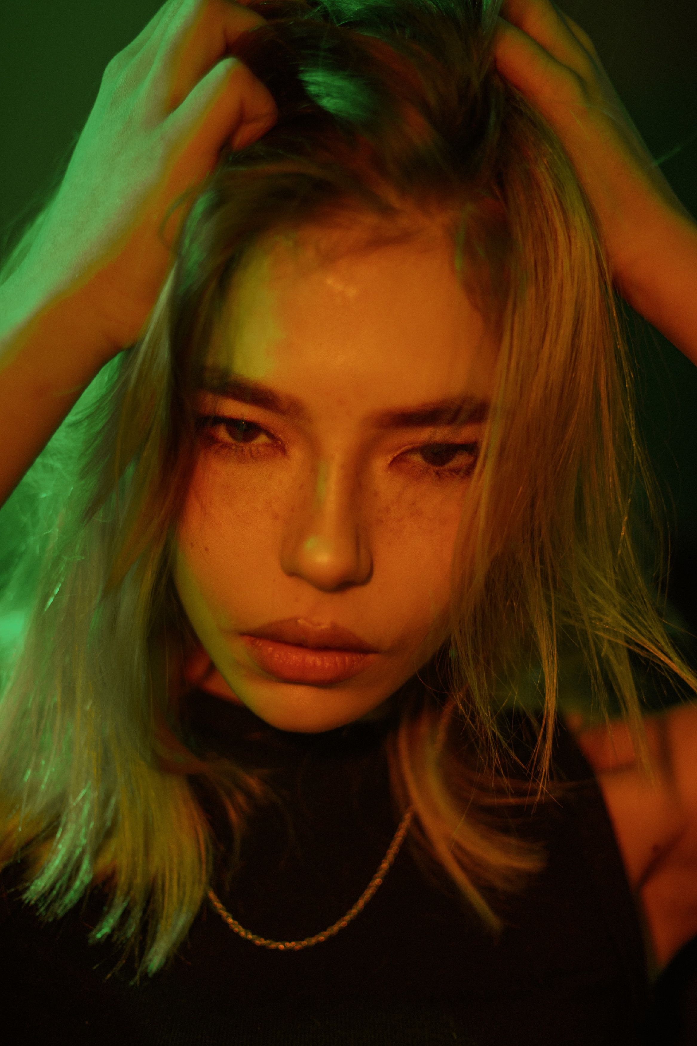 Dramatic close-up portrait of a woman adjusting her blonde hair, captured with artistic lighting.