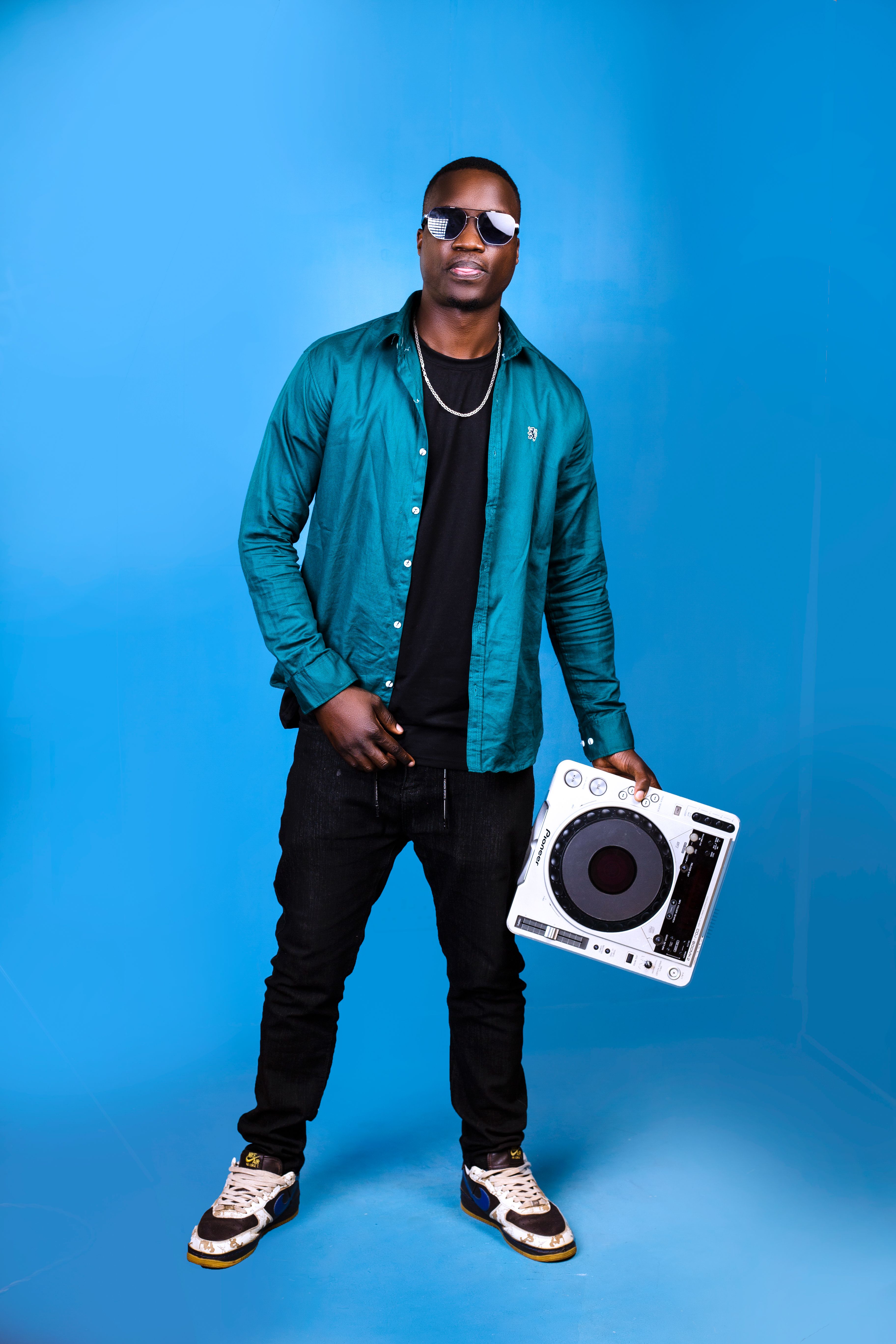 Stylish man in sunglasses holding DJ mixer against blue studio background.