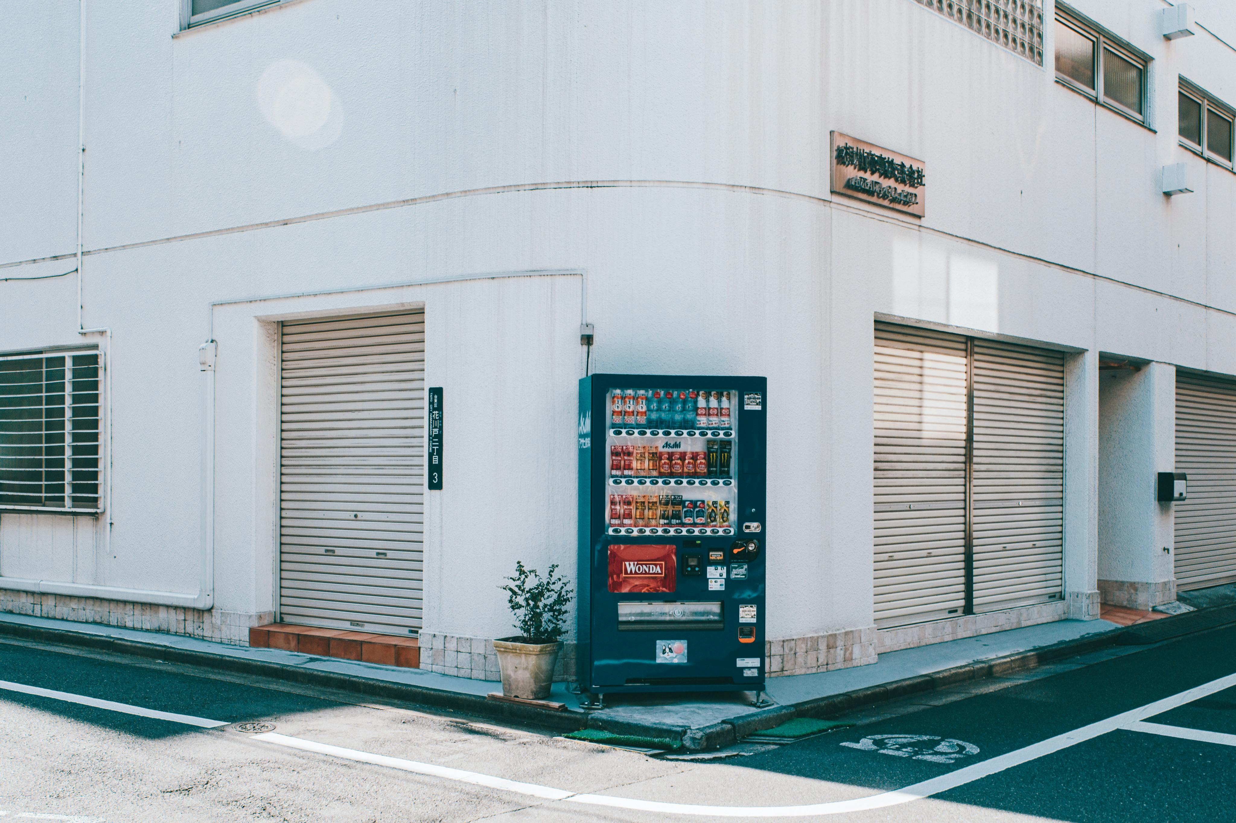 Free A quiet urban street corner featuring a vending machine against a white building. Stock Photo