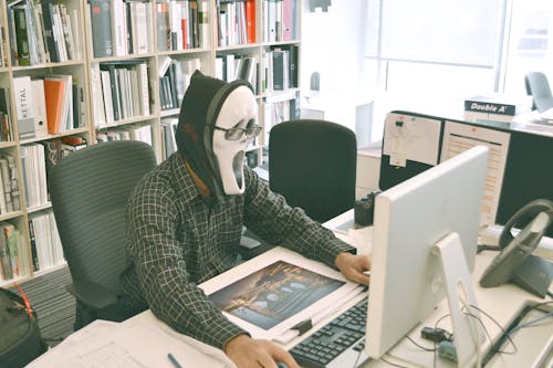 Gratis Persona Che Indossa Una Maschera Da Urlo E Una Camicia Nera Mentre Si Trova Di Fronte Al Tavolo Del Computer Durante Il Giorno Foto a disposizione