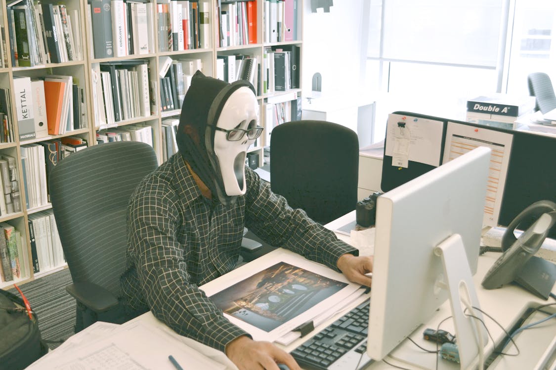 白天面对计算机桌时，戴着尖叫面具和黑色礼服衬衫的人