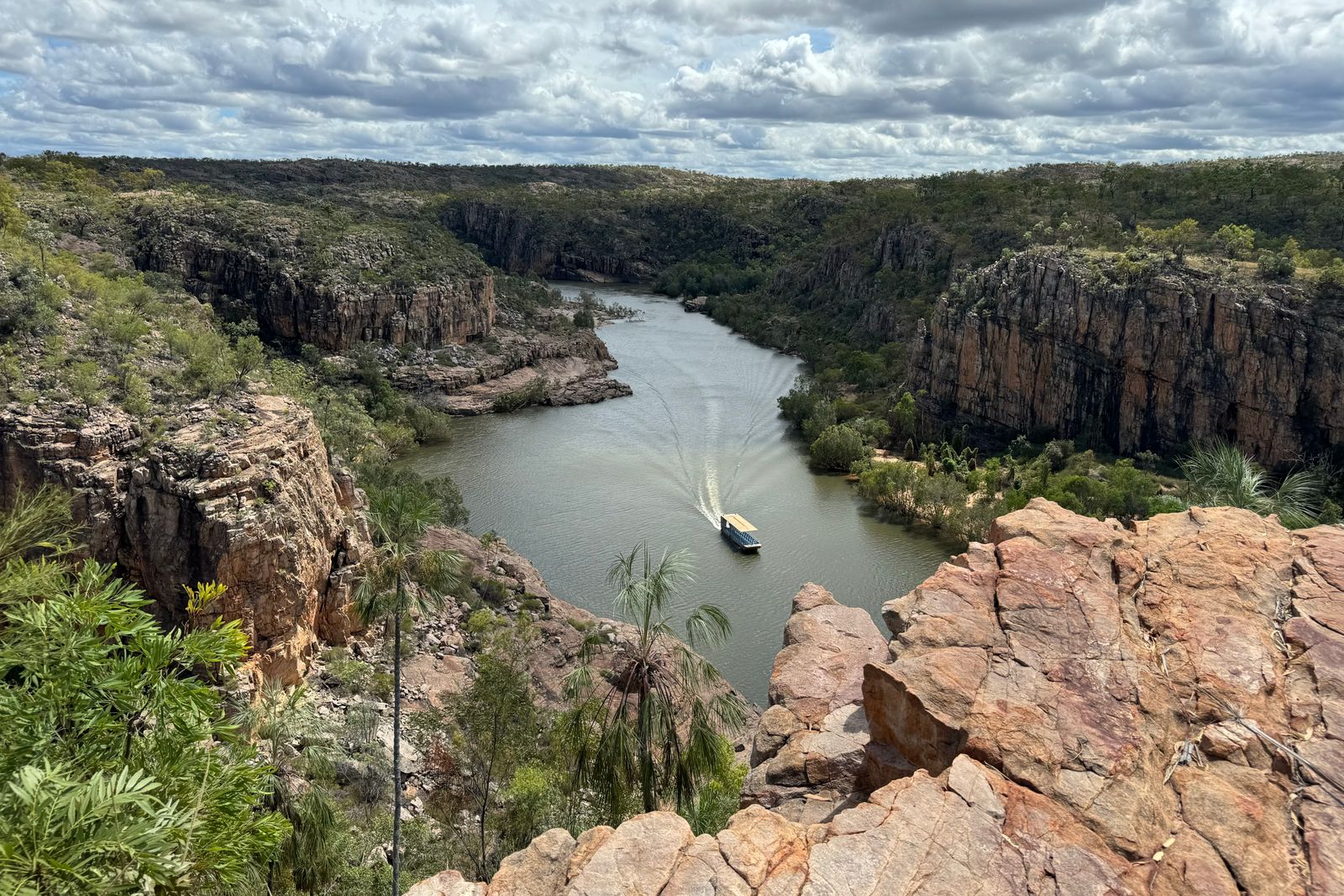 A small boat running between red sandstone cliffs along a river gorge in Australia's Kimberley.