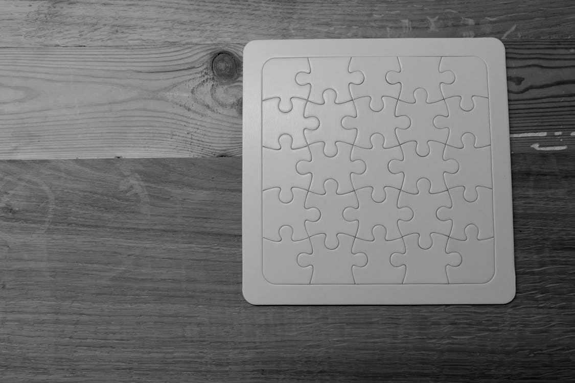 White and Black Puzzle Piece on Brown Wooden Table