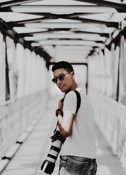 一位年轻摄影师戴着太阳镜，手持相机，站在一座现代桥上