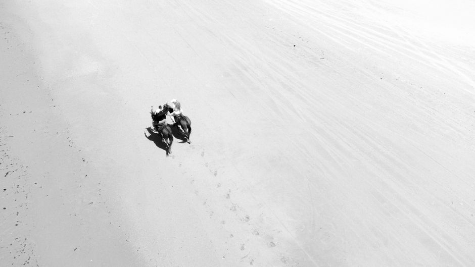 Aerial black and white photo of people riding horses on Flecheiras Beach.