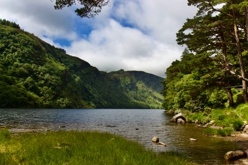 Free Beautiful lake surrounded by lush greenery and mountains under a partly cloudy sky. Stock Photo