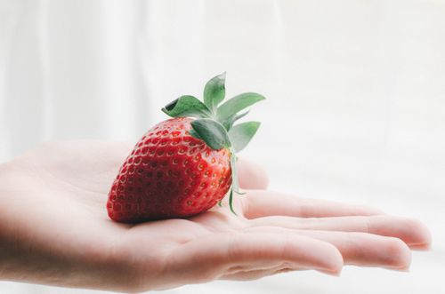 Free A fresh red strawberry held in an open palm against a light, soft background. Perfect for food and lifestyle themes. Stock Photo