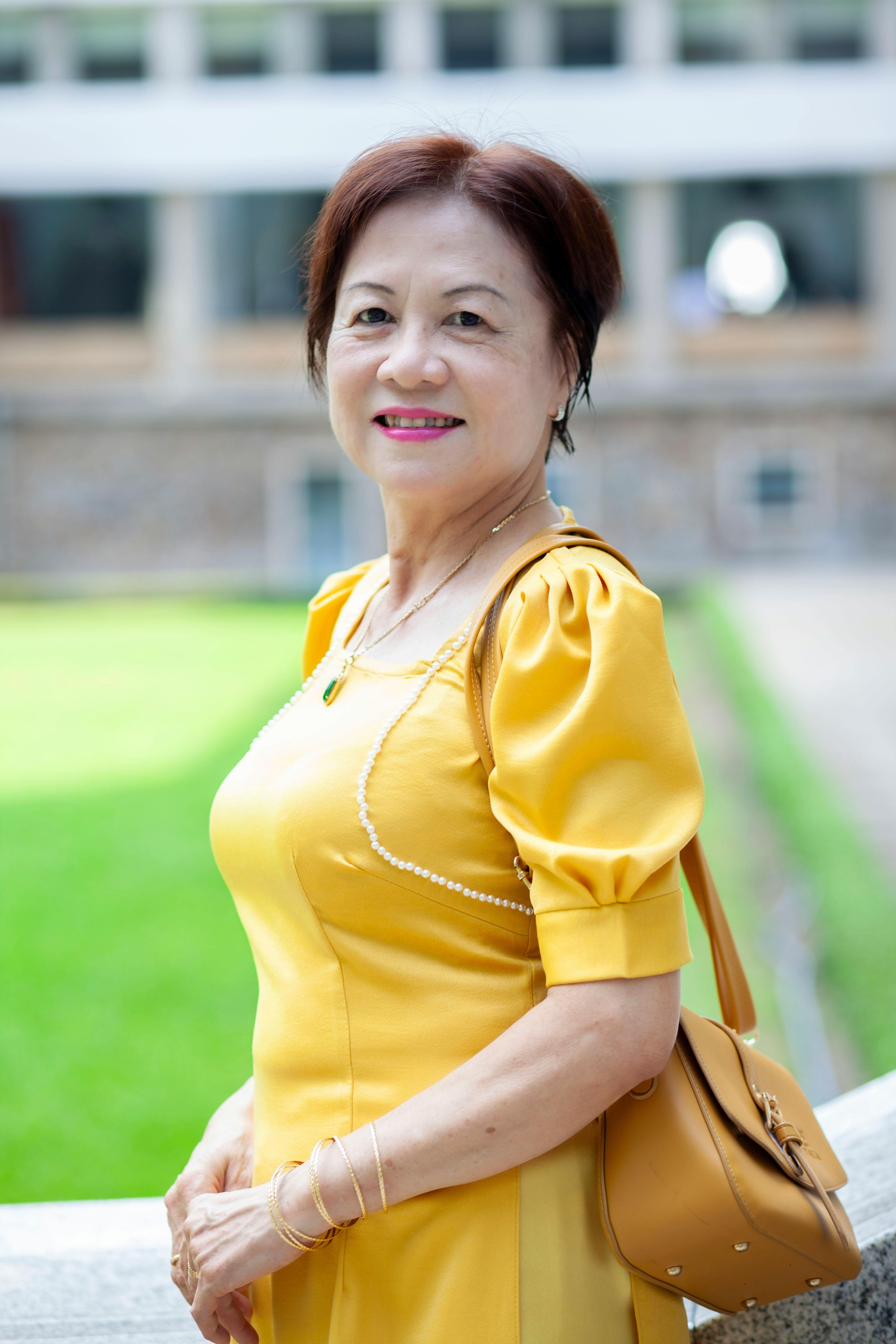 An elegant woman in a yellow dress poses in an urban outdoor setting.