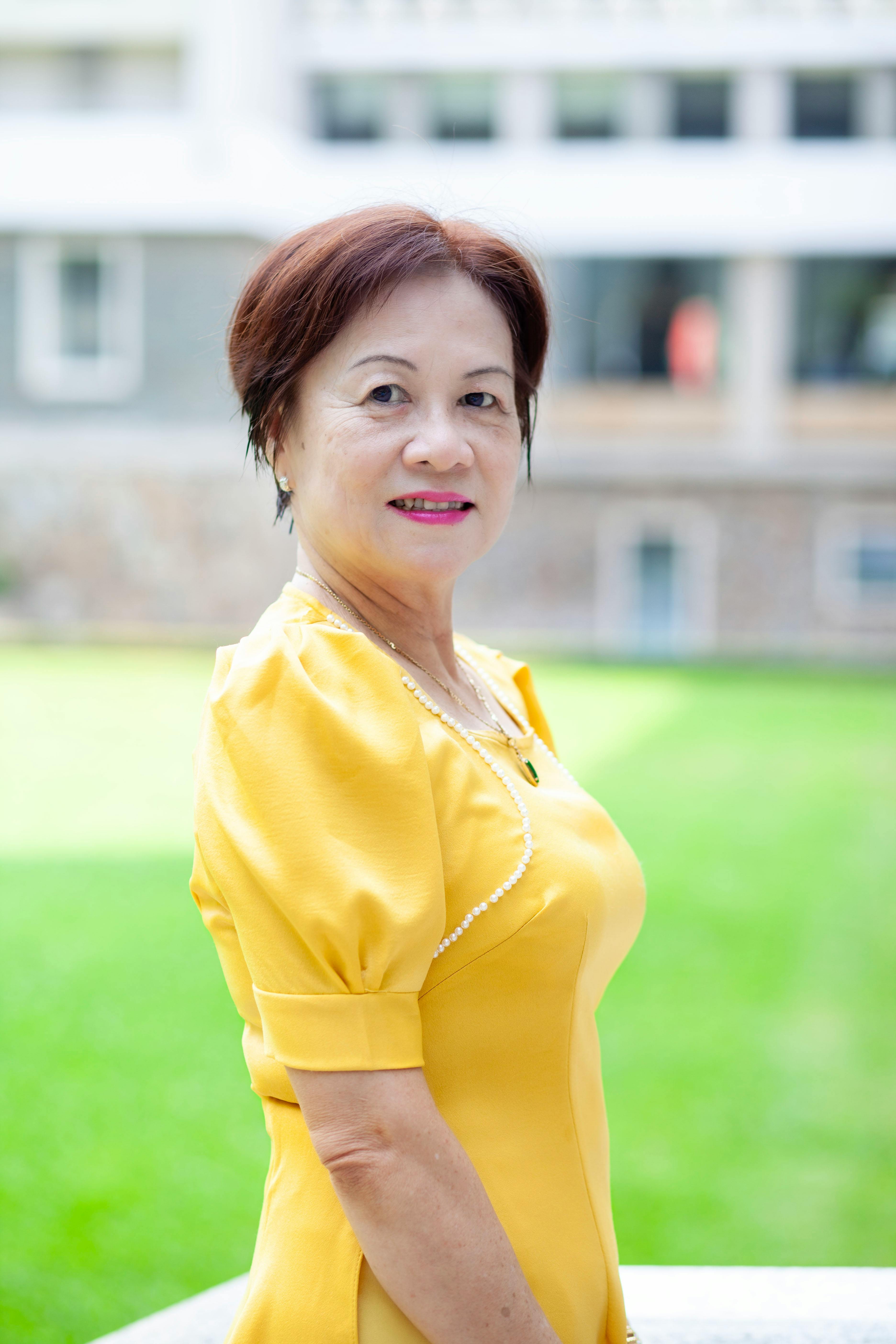 Portrait of an elegant mature woman standing outdoors in a bright yellow dress with a blurred urban background.