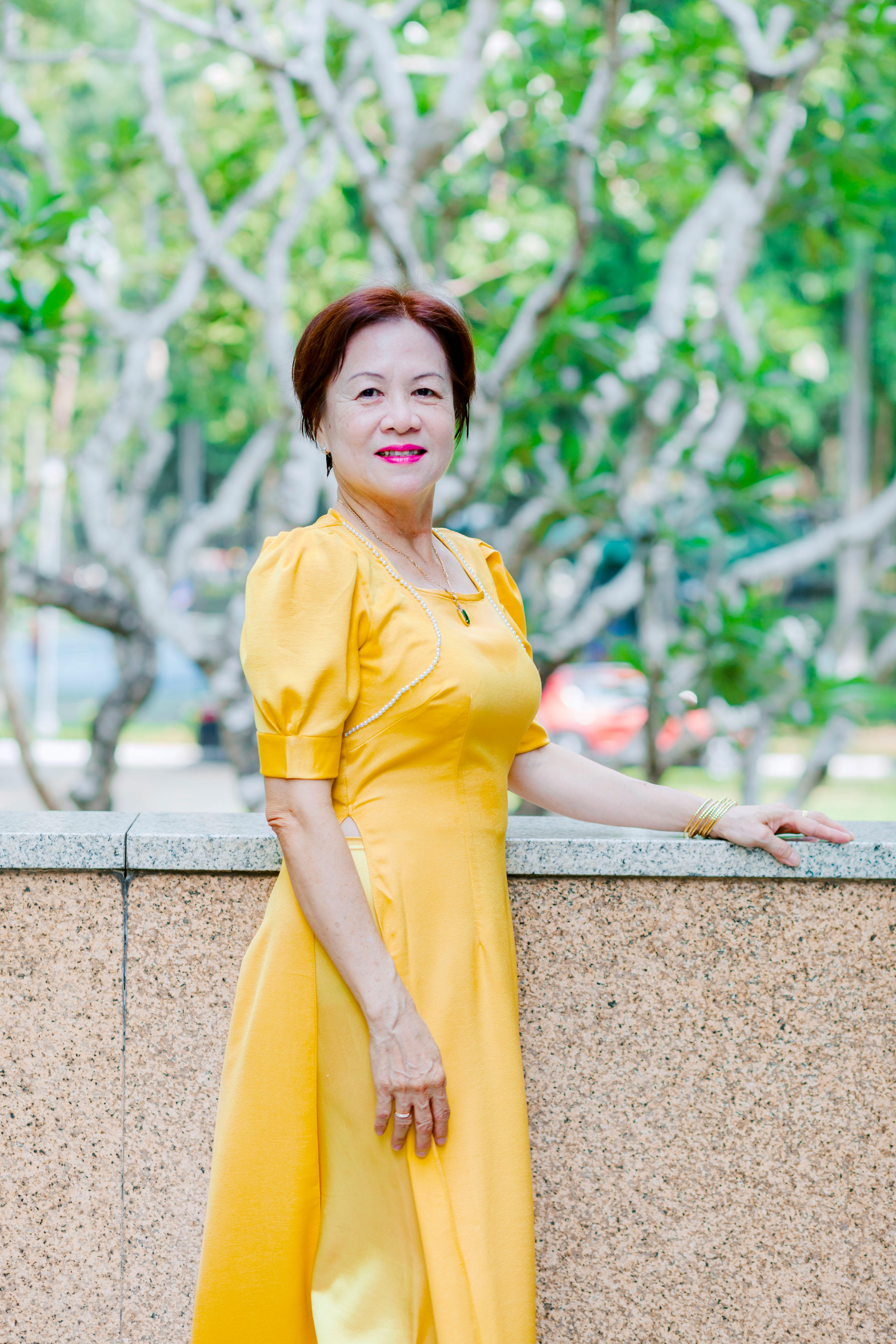 Portrait of an elegant woman in a traditional yellow dress, enjoying a sunny day in the park.