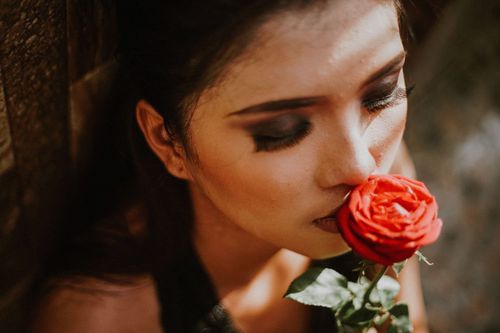 Free Close-up of a woman smelling a red rose in warm sunlight, creating a romantic mood. Stock Photo