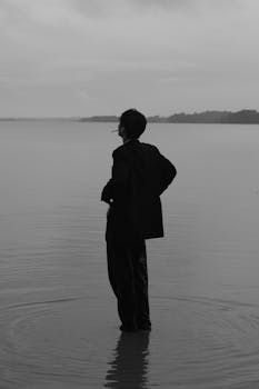 Silhouette of a person standing in water, gazing at the horizon, conveying solitude and reflection.