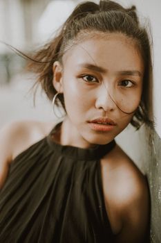 Close-up portrait of a woman leaning against a wall with messy hair and hoop earrings.