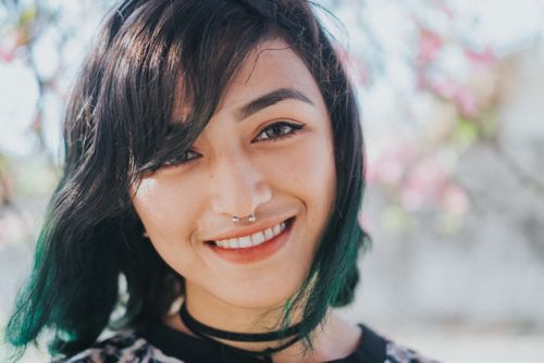 Free Close-up portrait of a young woman with green hair and a nose ring, smiling outdoors. Stock Photo