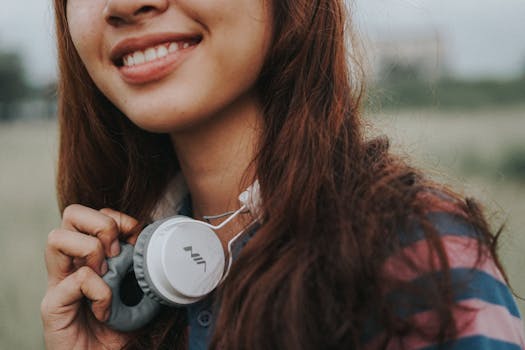 A close-up of a young woman smiling while holding headphones in an outdoor setting.