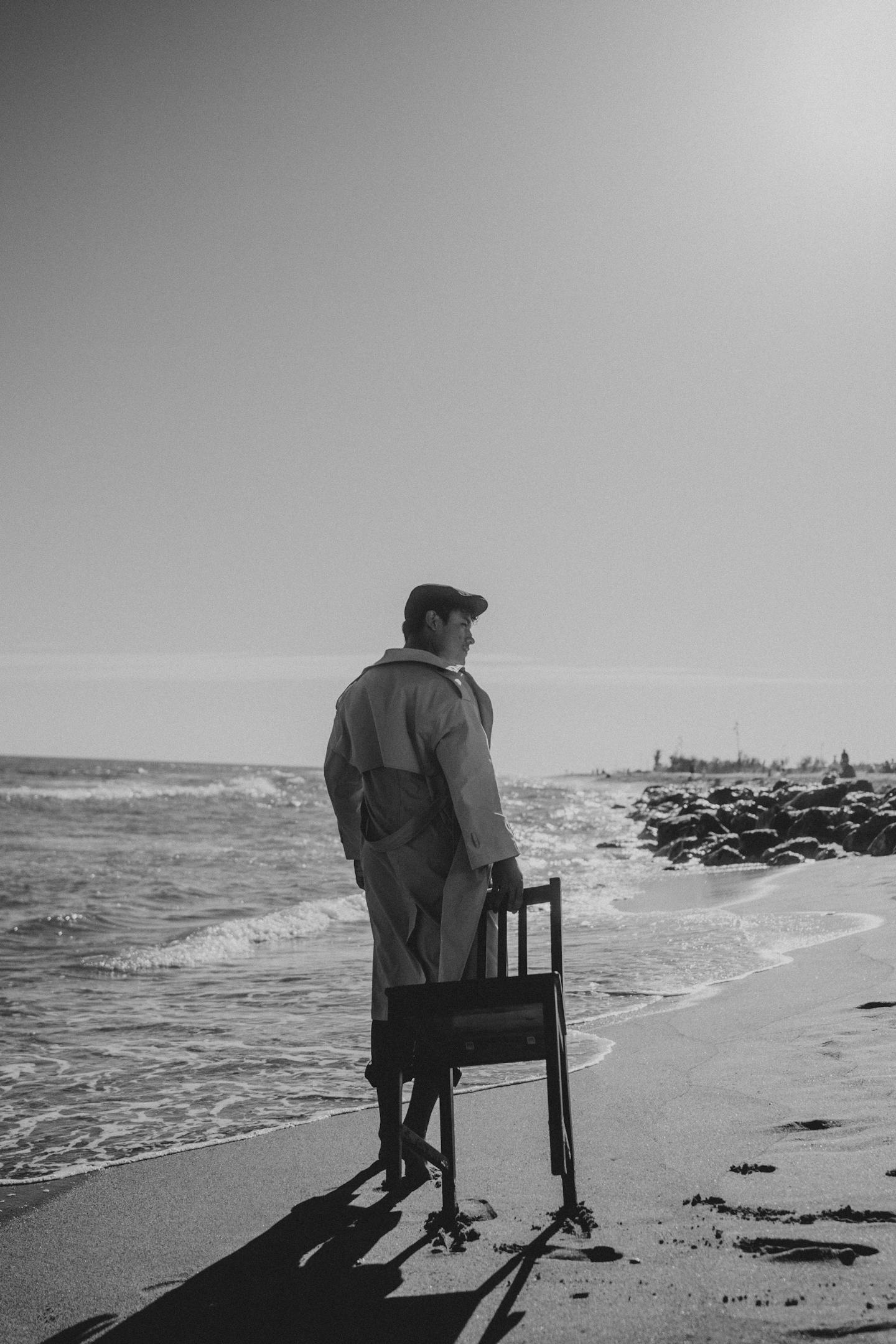 Free Man Walking with Chair on Sea Shore in Black and White Stock Photo