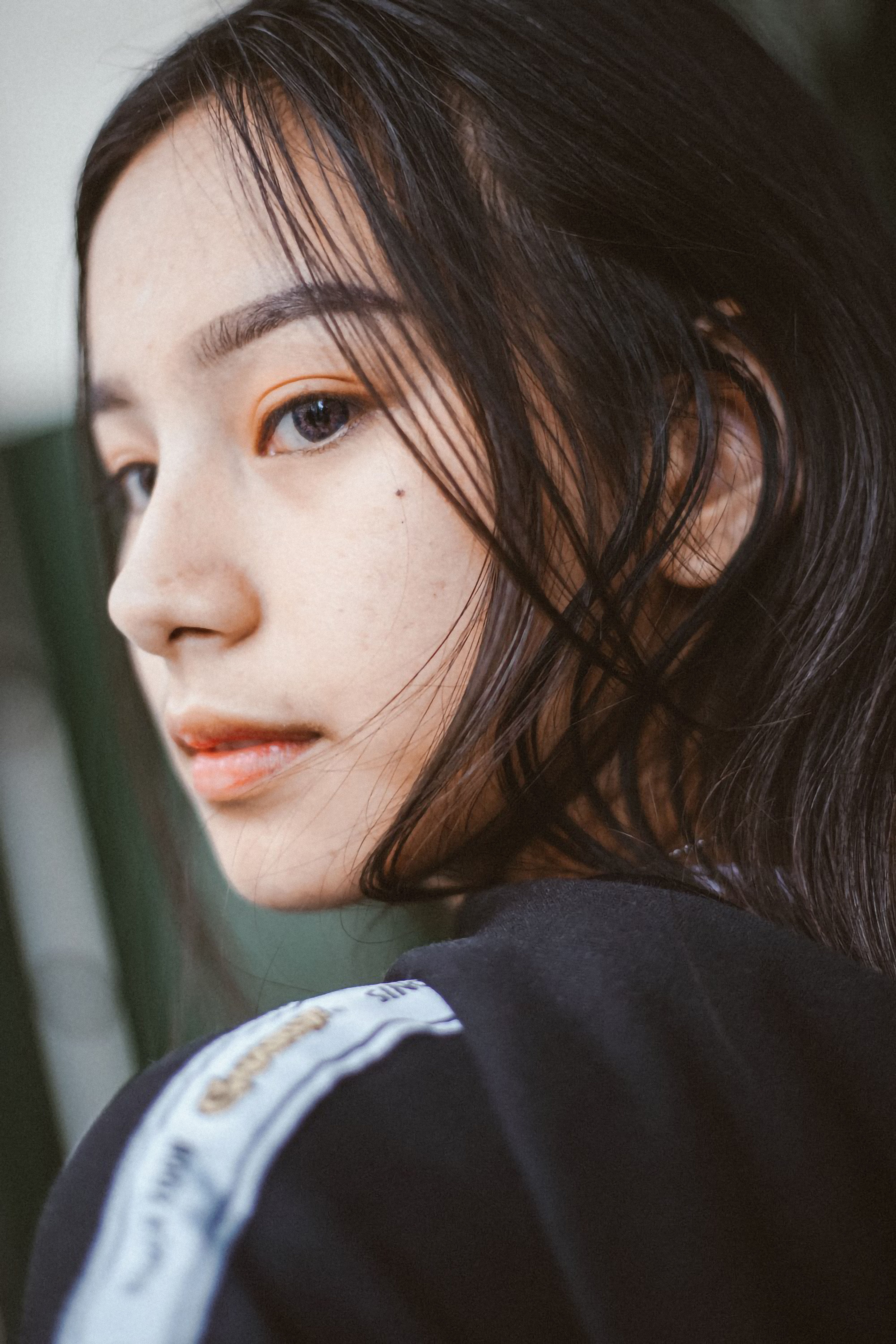 A close-up side portrait of an adult woman with long black hair and freckles.