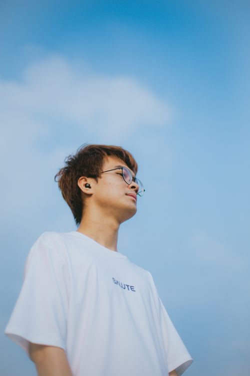 Free Portrait of a young man wearing eyeglasses and headphones looking up under a bright blue sky in Thái Nguyên, Vietnam. Stock Photo