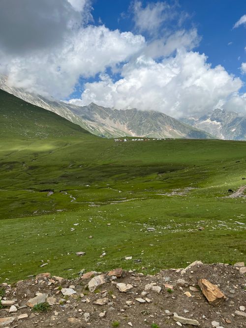 Free Scenic view of lush green meadows and mountain range under a partly cloudy sky. Stock Photo