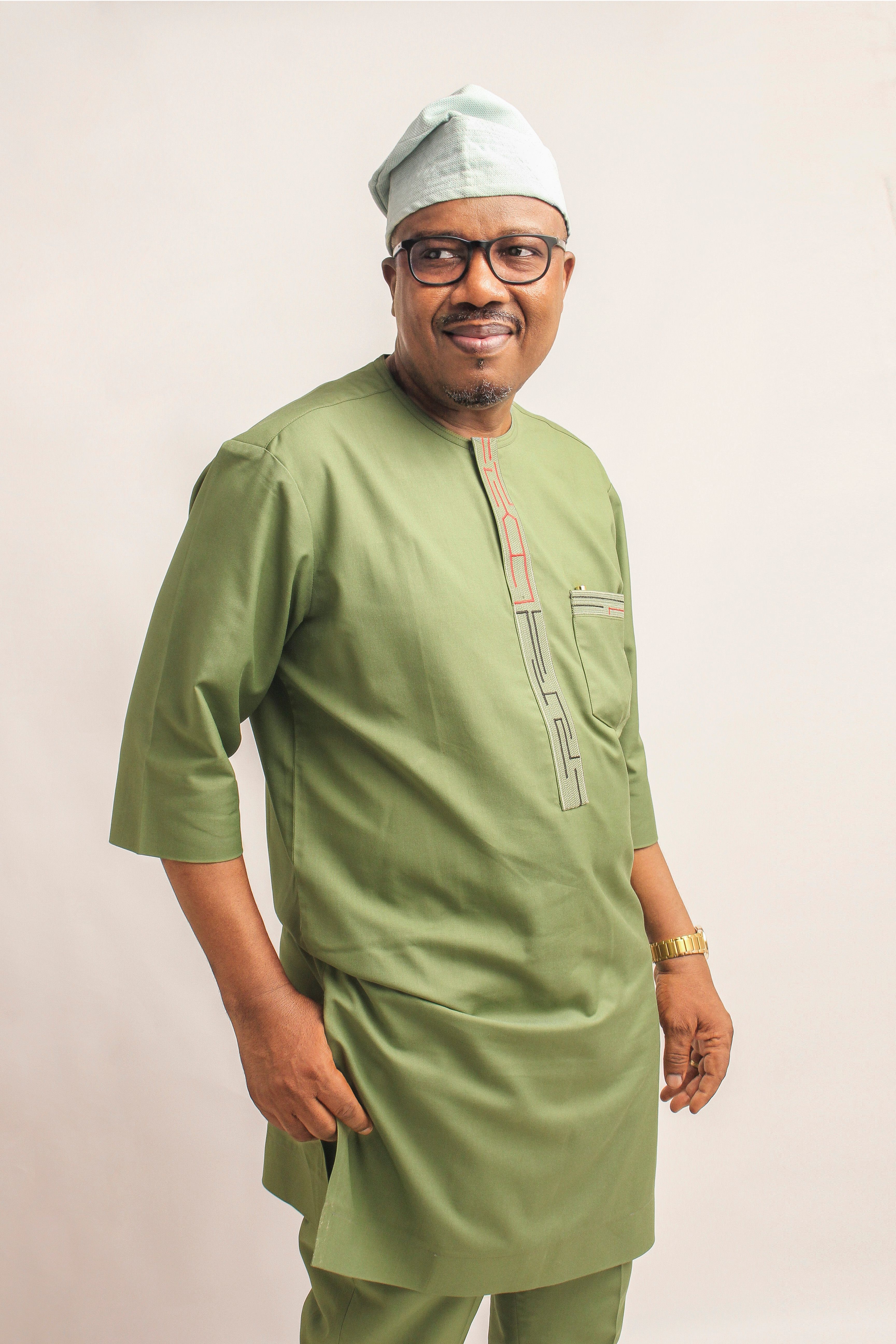 Portrait of a stylish man wearing traditional green attire, smiling in a studio shot.