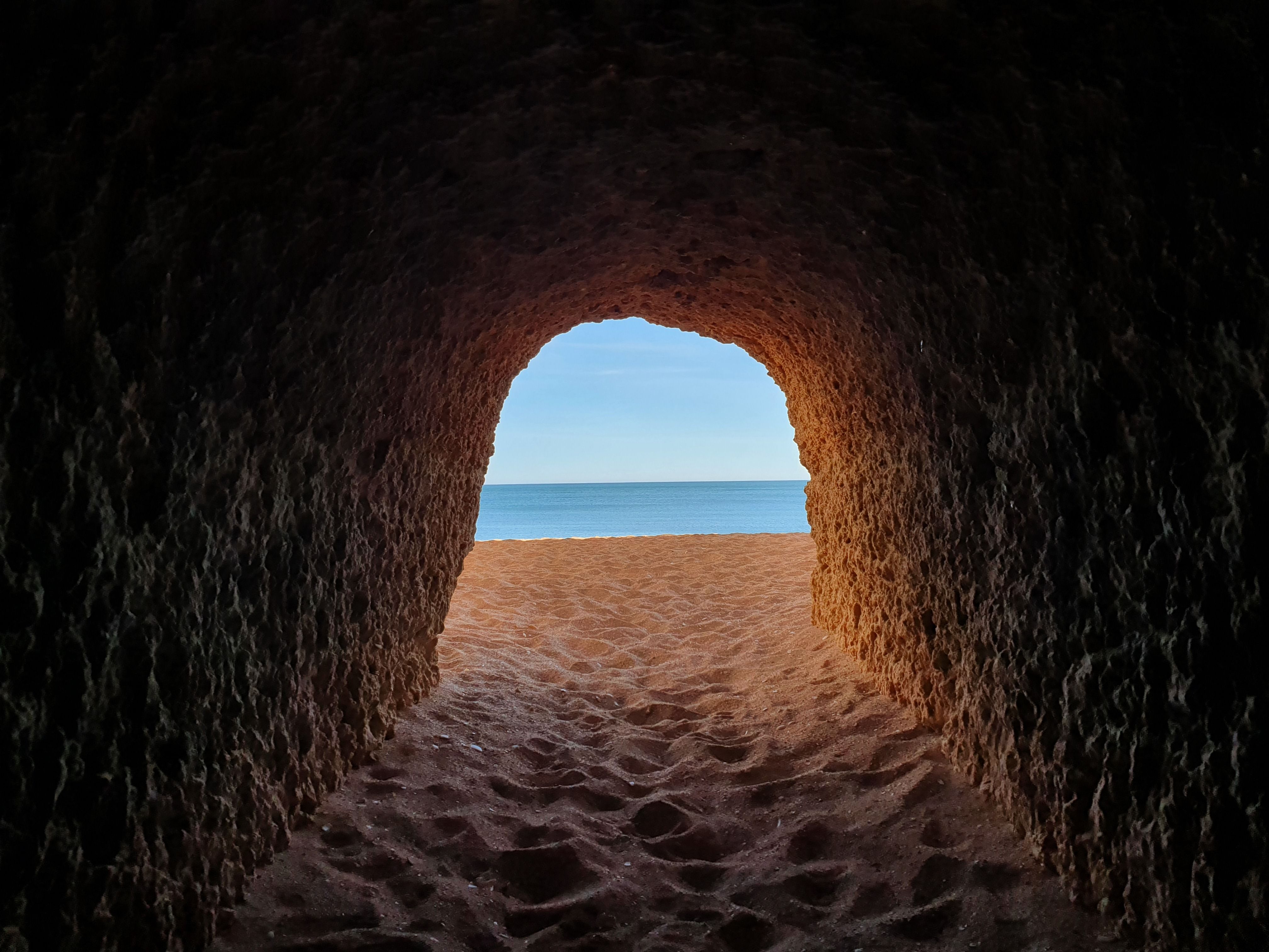 View from a cave tunnel leading to a pristine Algarvia beach in Portugal under a clear sky.