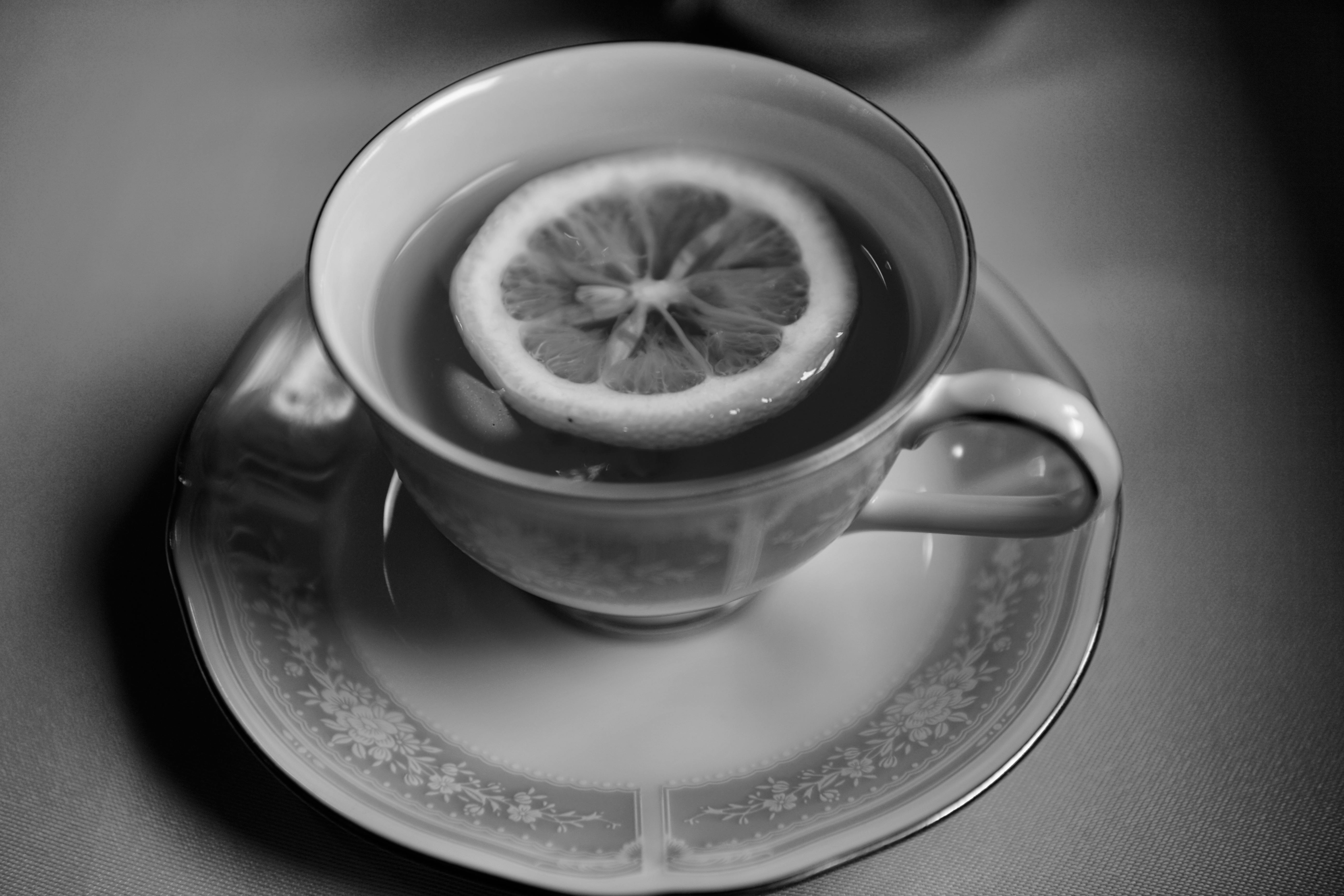 Black and white image of tea with a slice of lemon in a delicate porcelain cup with saucer.