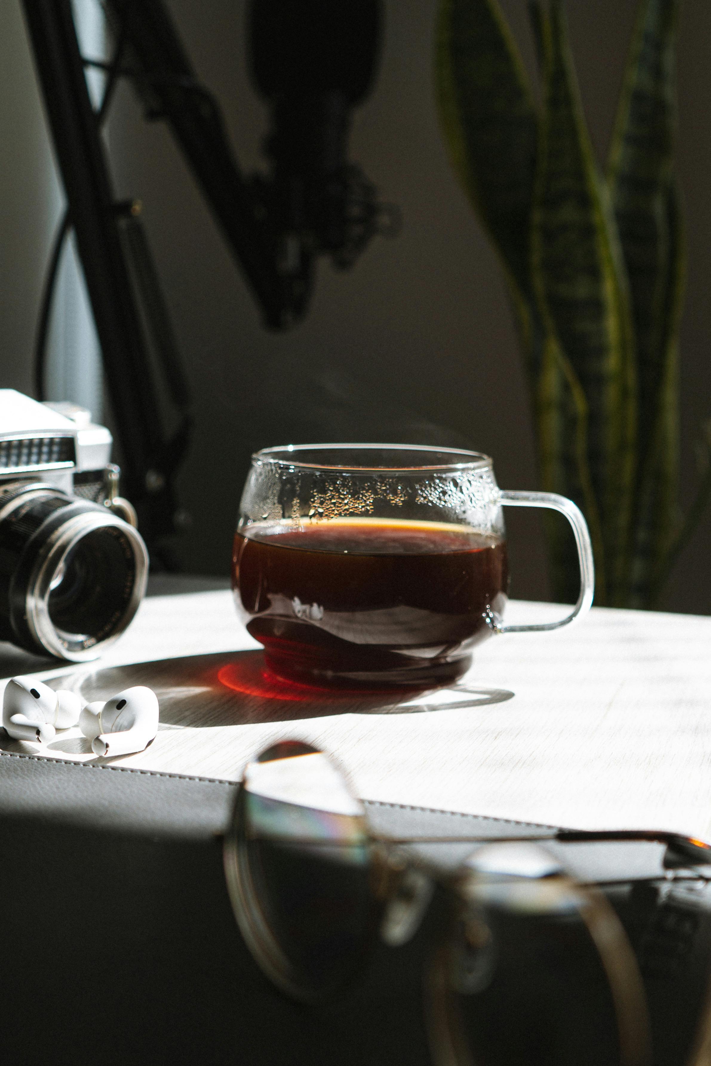 A glass of coffee on a table with camera, earphones, and glasses, perfect for creative workspace.