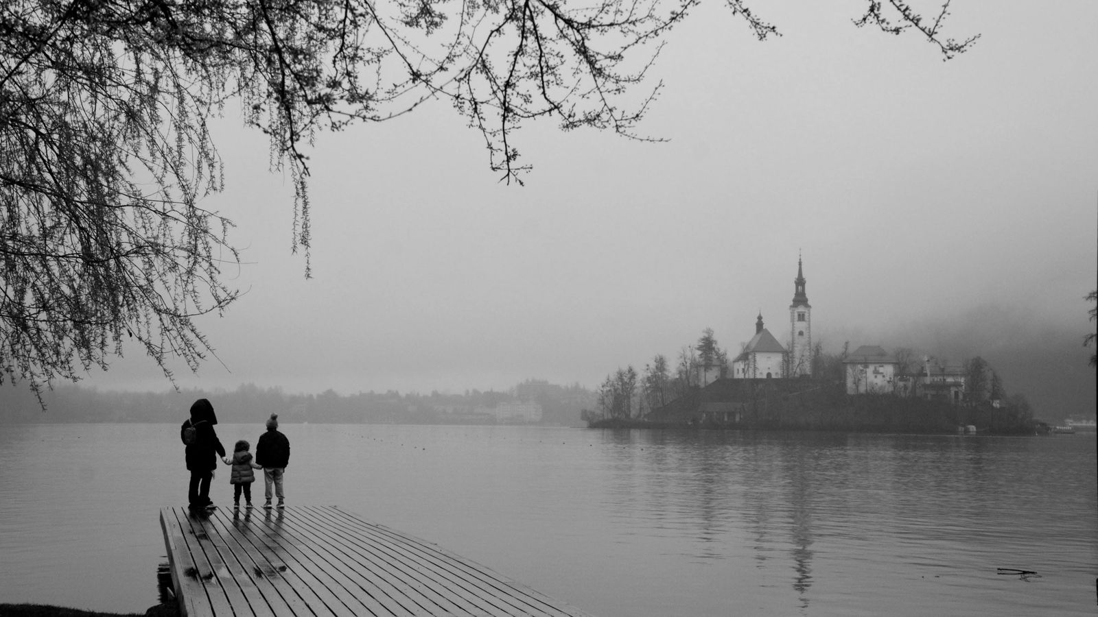 Family standing on a pier and looking across Lake Bled