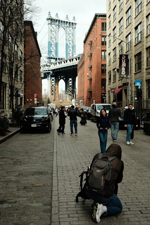 A man is kneeling on the ground in front of a manhattan bridge