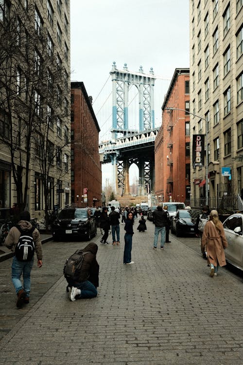 People walking down a city street with the manhattan bridge in the background