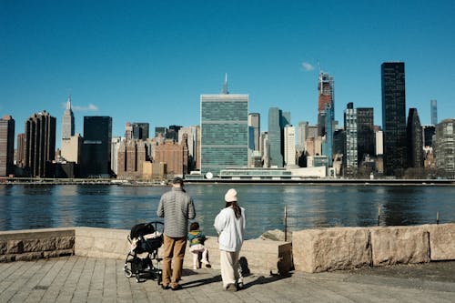 A man and woman are walking on the waterfront with the new york city skyline in the background
