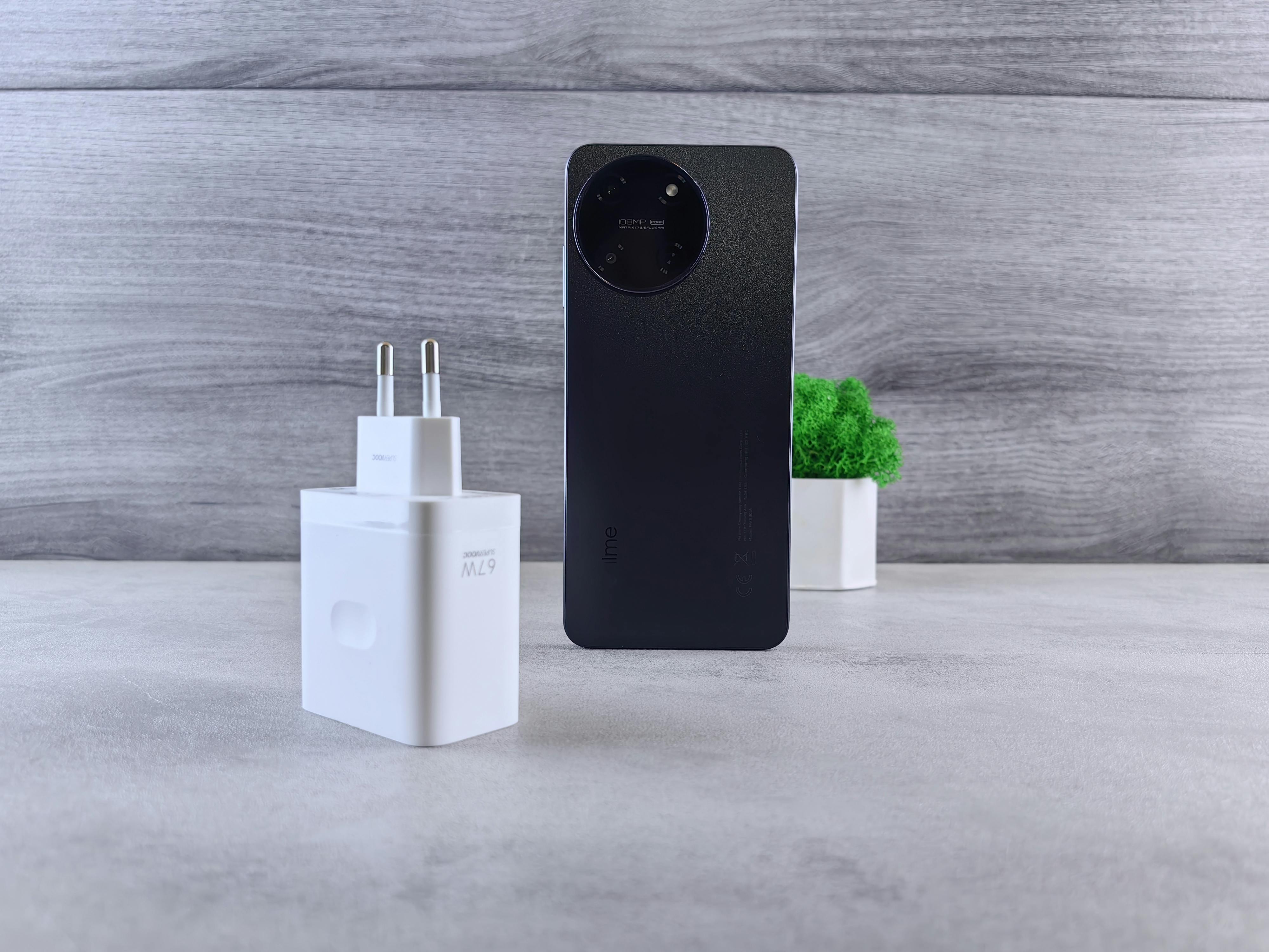 Minimalist composition of a smartphone, charger, and small green plant on a grey background.