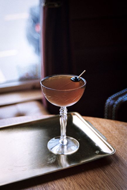 A refined cocktail in a crystal glass sits on a golden tray by a window, capturing elegance.