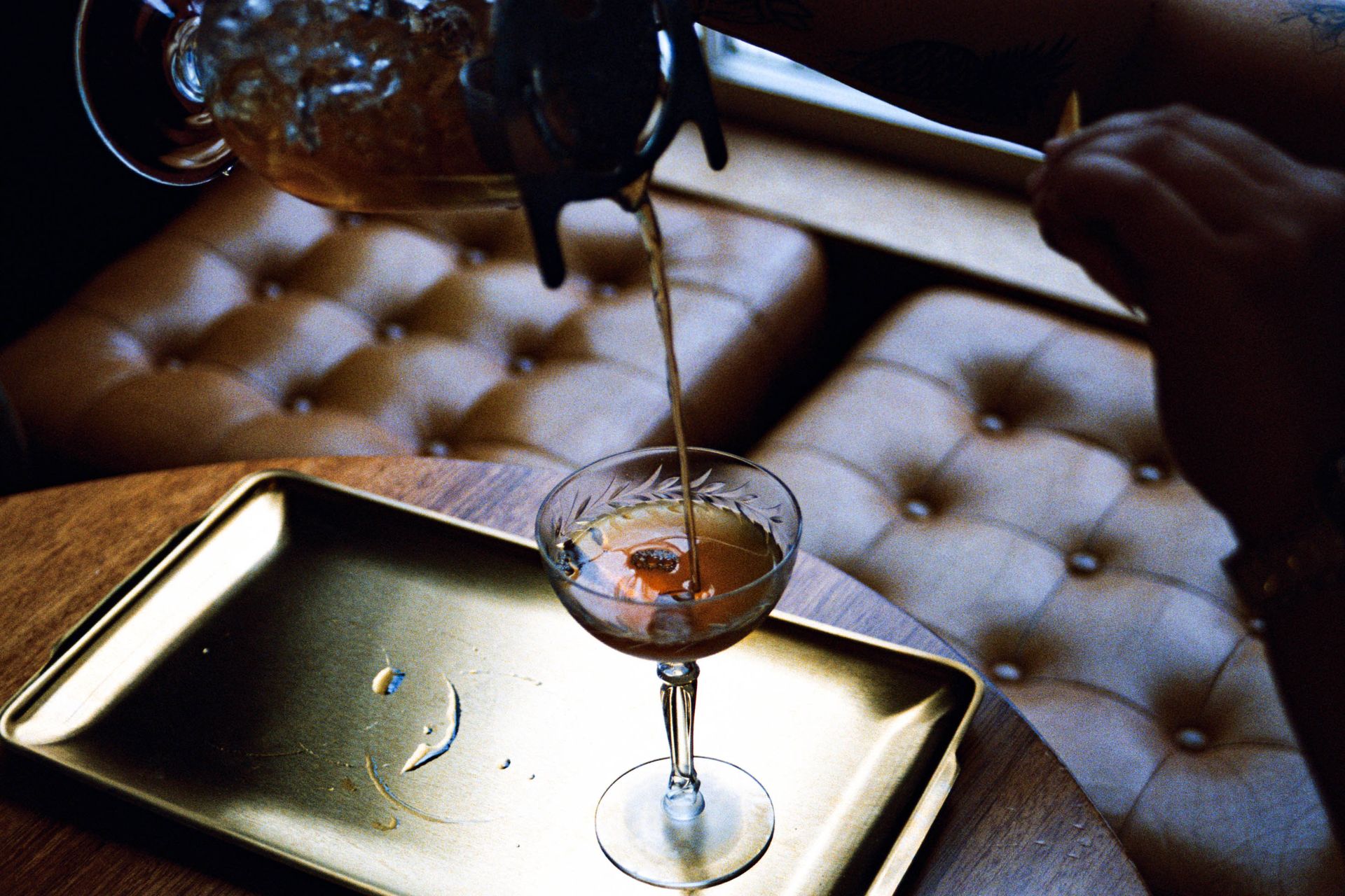 A handcrafted cocktail being poured into an elegant coupe glass on a tray, ready to serve.