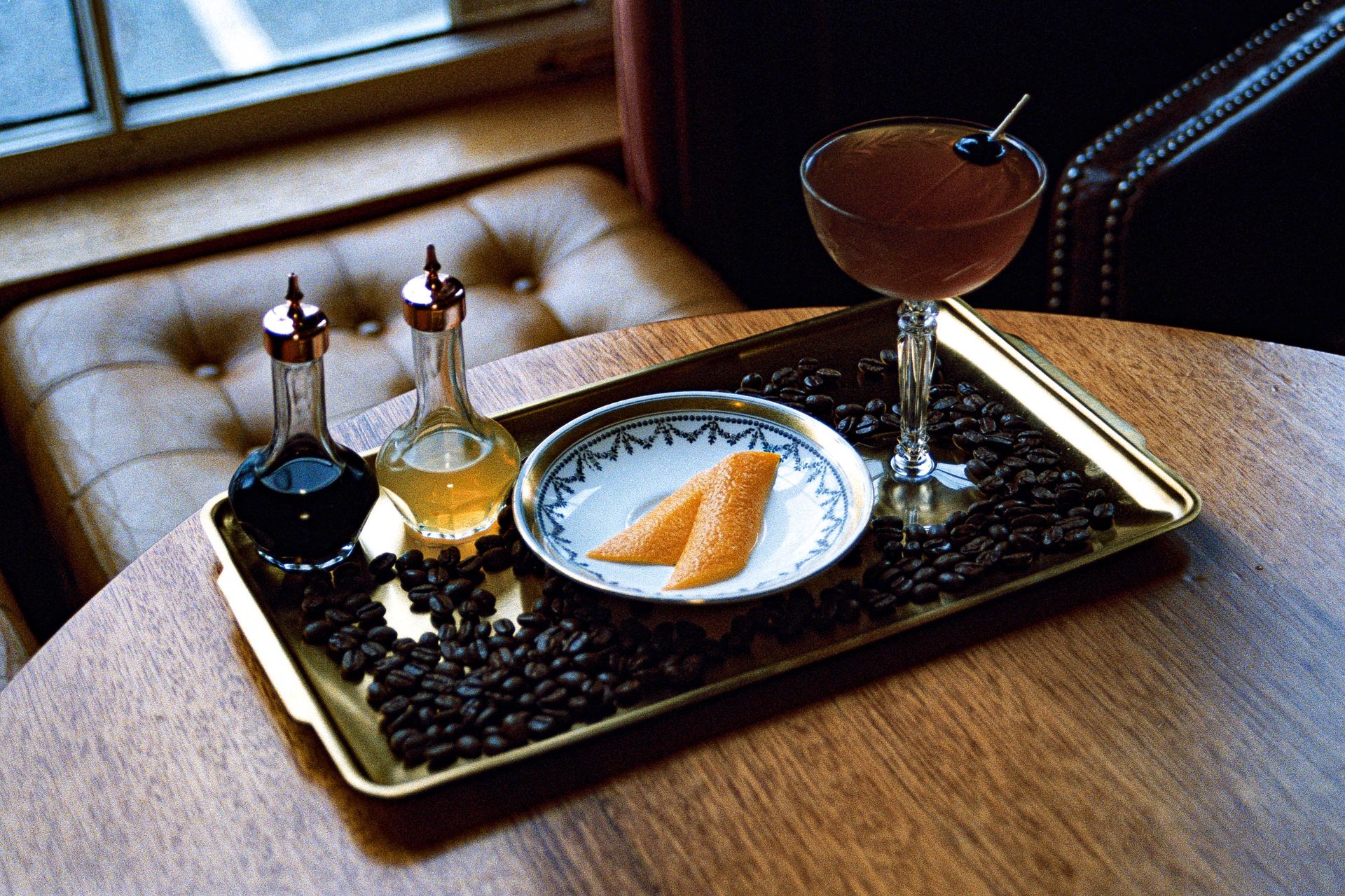 A sophisticated cocktail served on a tray with coffee beans and citrus garnish, exuding a classic vibe.