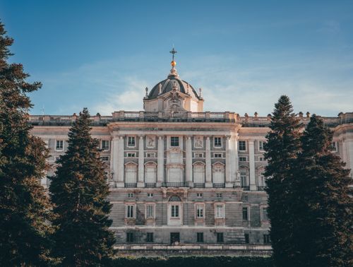 Free Stunning view of the Royal Palace of Madrid with neoclassical architecture framed by trees. Stock Photo